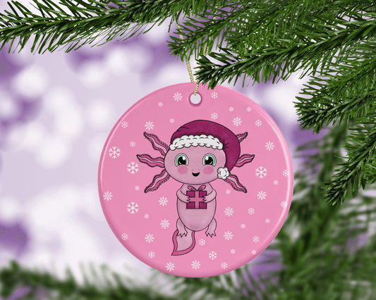 A round ceramic Christmas decoration to hang from a tree. Has a hand drawn illustration of a cute axolotl wearing a Santa hat and holding a Christmas gift. The bauble has a pink snowy background.
