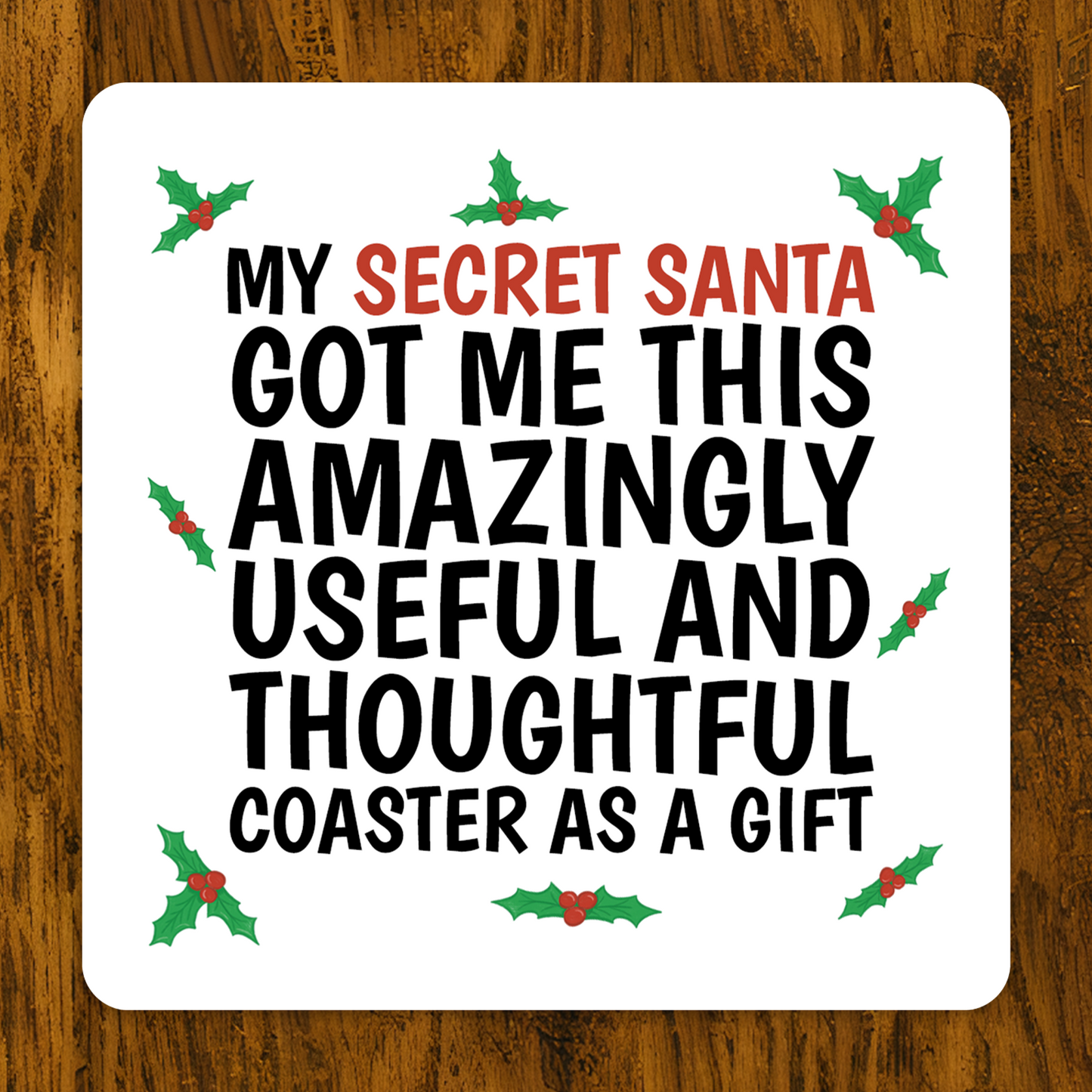 Coaster with Christmas-themed text on a wooden surface .Funny Secret Santa coaster with holly design and text “My Secret Santa got me this amazingly useful and thoughtful coaster as a gift.”
