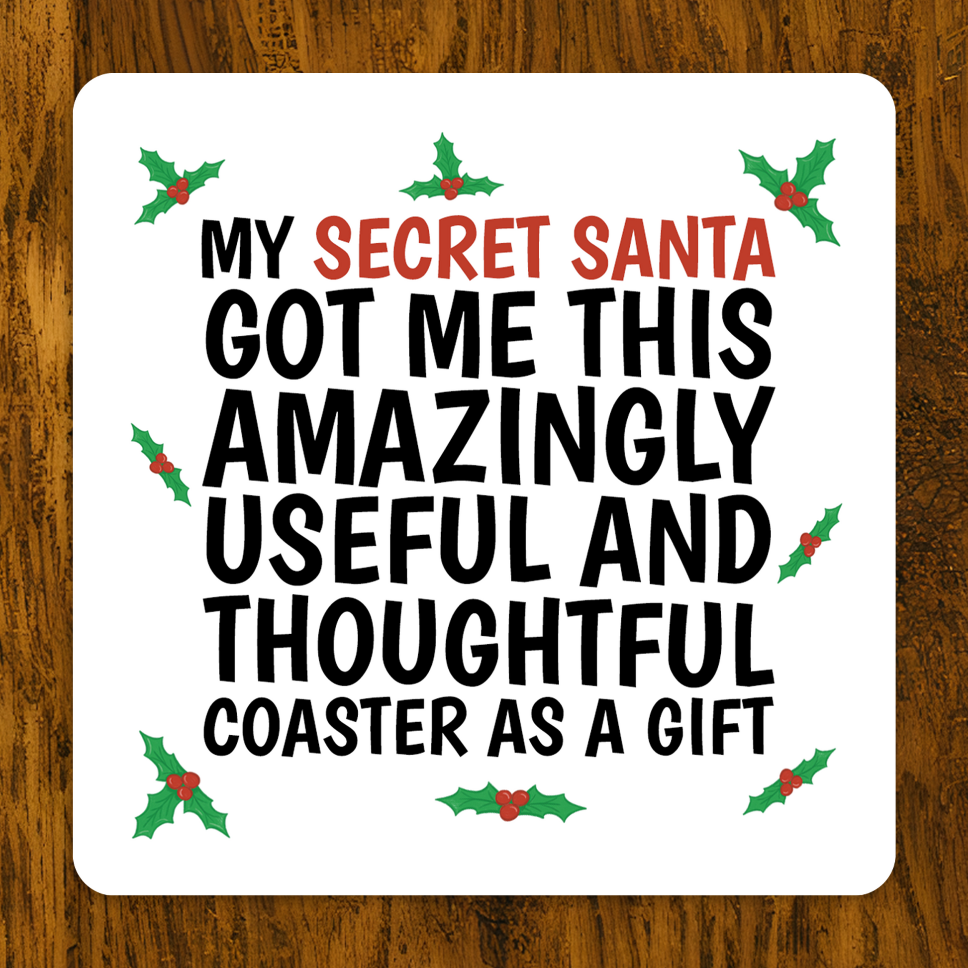 Coaster with Christmas-themed text on a wooden surface .Funny Secret Santa coaster with holly design and text “My Secret Santa got me this amazingly useful and thoughtful coaster as a gift.”