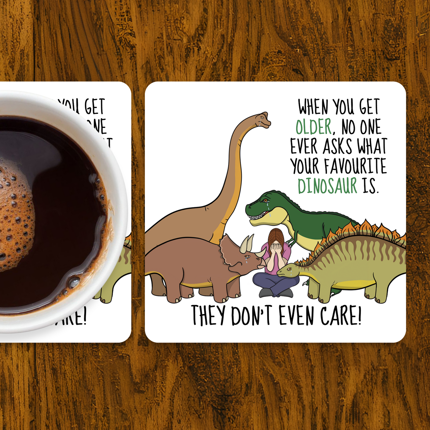 Two coasters with dinosaur illustrations and humorous text on a wooden surface with a cup of coffee.